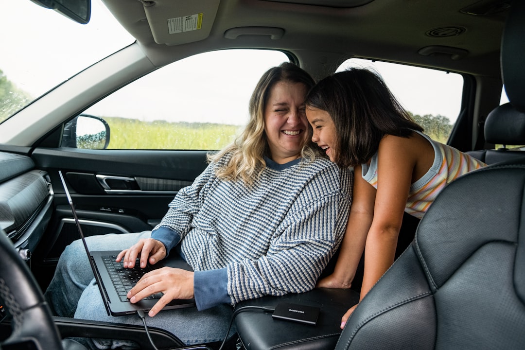Woman works on laptop with child in car.